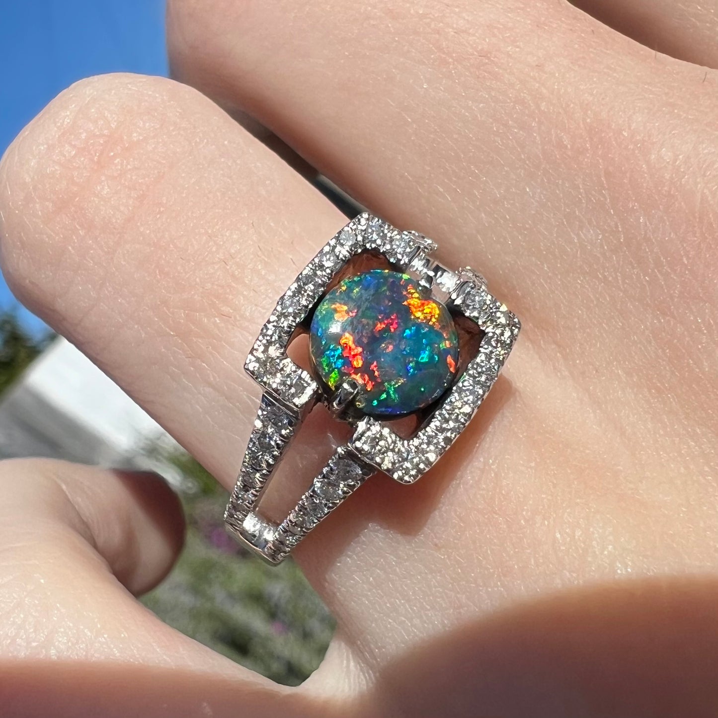 A close-up angled shot of a Lightning Ridge black opal engagement ring in natural light, showcasing intense red multicolor fire. Set in 14k white gold with diamonds by Luciano Bortone.