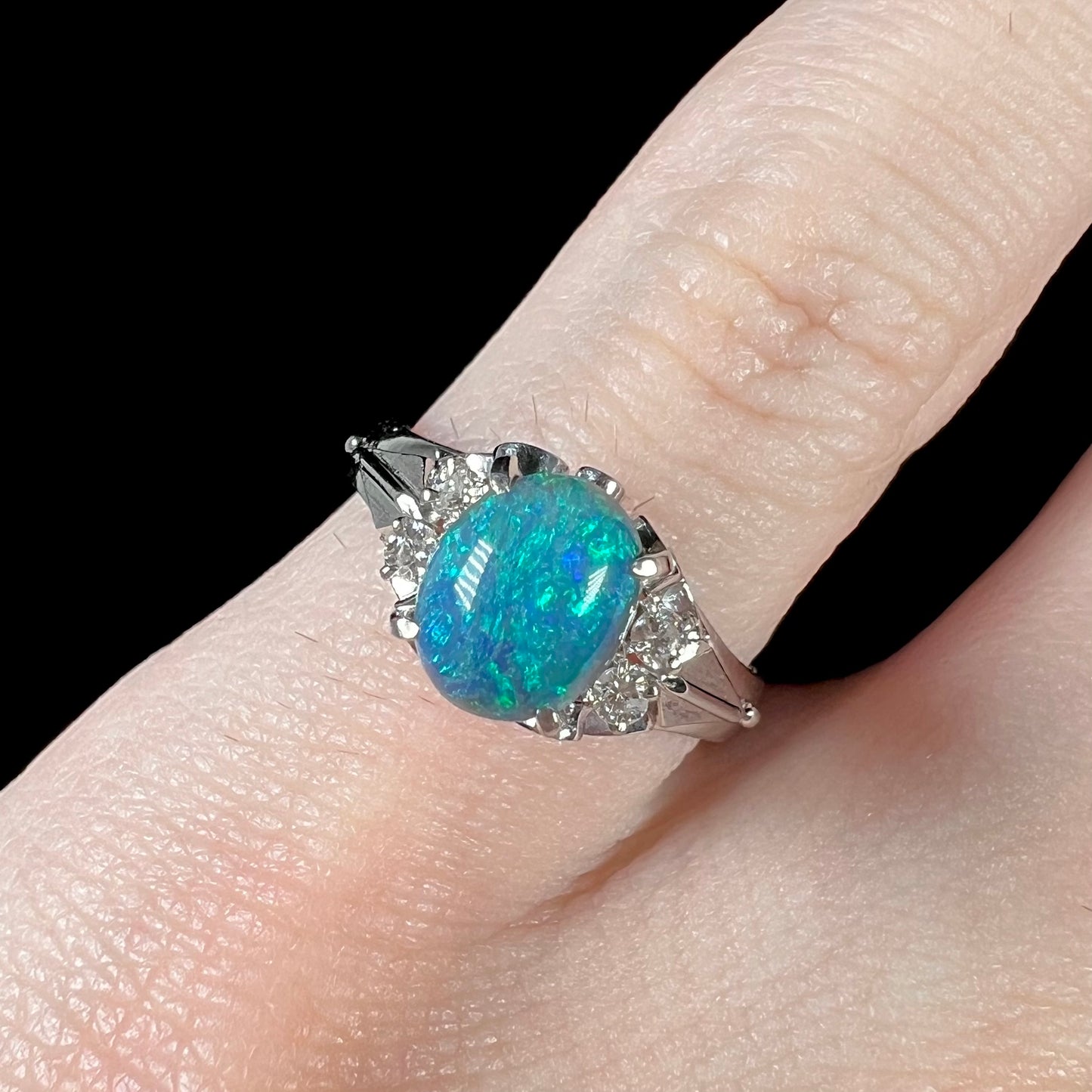 A 0.89ct Lightning Ridge black opal engagement ring set in platinum with diamond accents on a finger.