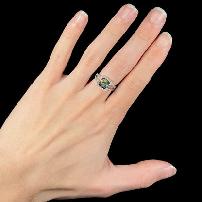 A round black opal engagement ring worn on a hand.  The ring's shape is square with diamond accents.