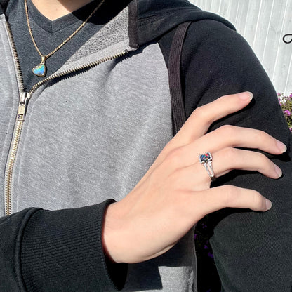 A Lightning Ridge black opal engagement ring worn on a model's hand in the sunlight.  Red colors are seen.