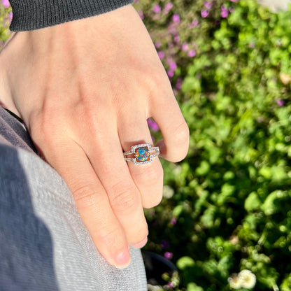 A Lightning Ridge black opal engagement ring photographed outdoors in natural light, showcasing vivid red and multicolor fire. Worn casually with a hand-on-hip pose. Set in 14k white gold with diamonds by Luciano Bortone.