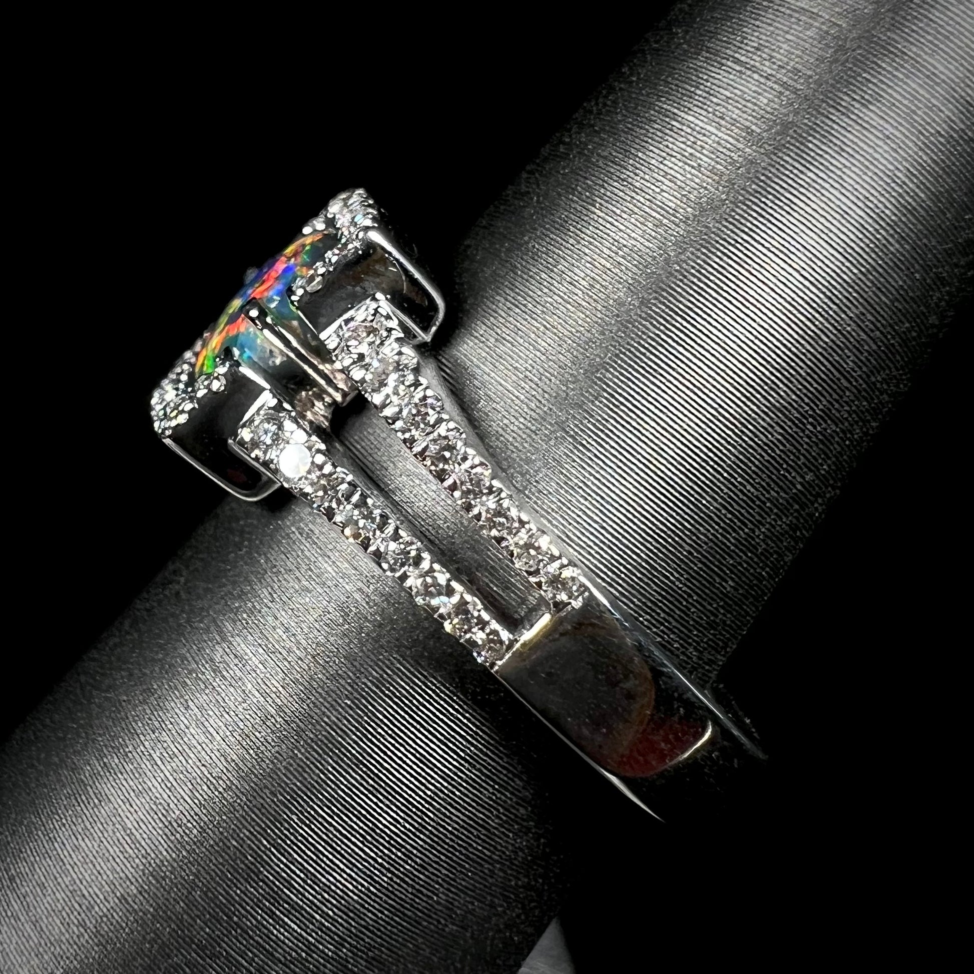 The side view of a black opal and diamond engagement ring.  Red colors show on the opal's exposed tip.