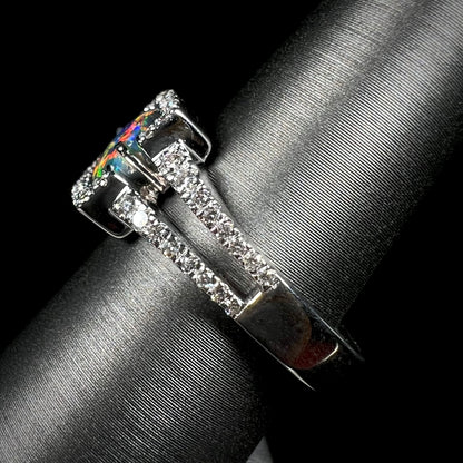 The side view of a black opal and diamond engagement ring.  Red colors show on the opal's exposed tip.