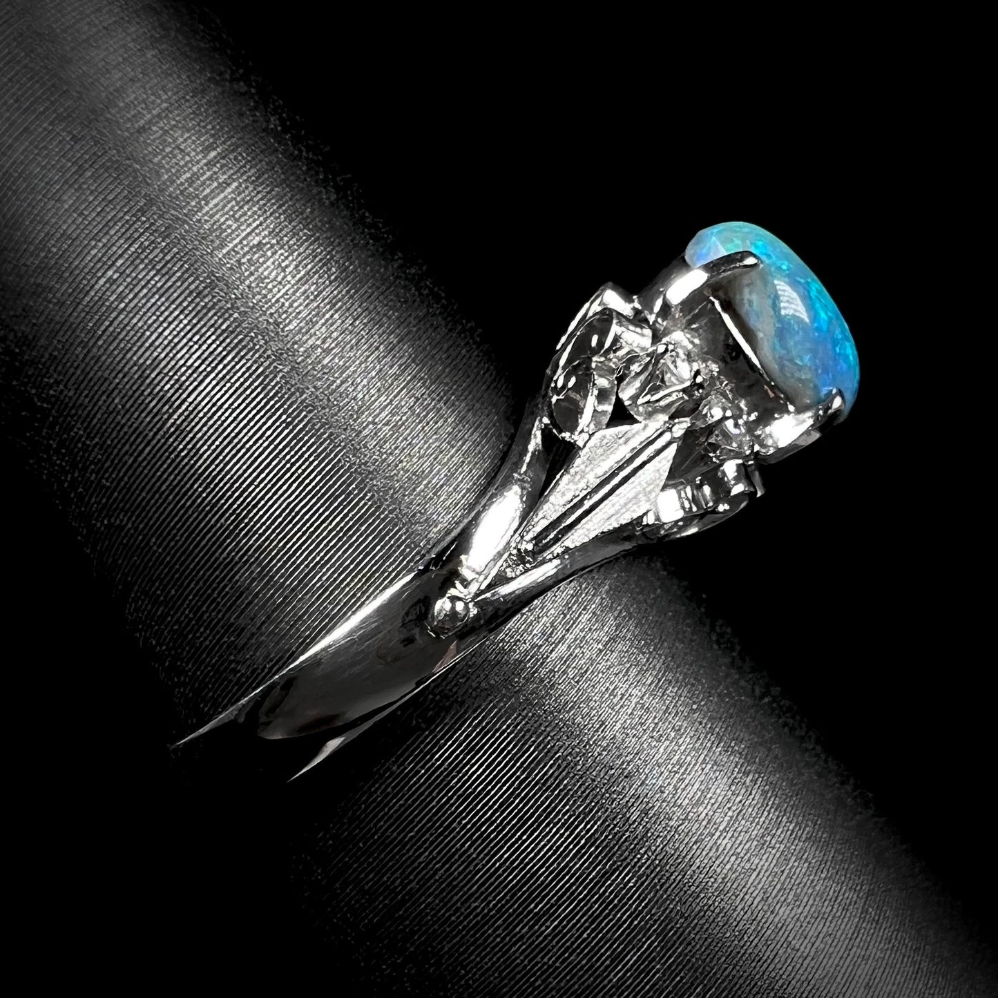 A side view of a platinum black opal engagement ring.  The opal shows blue colors and dark matrix.