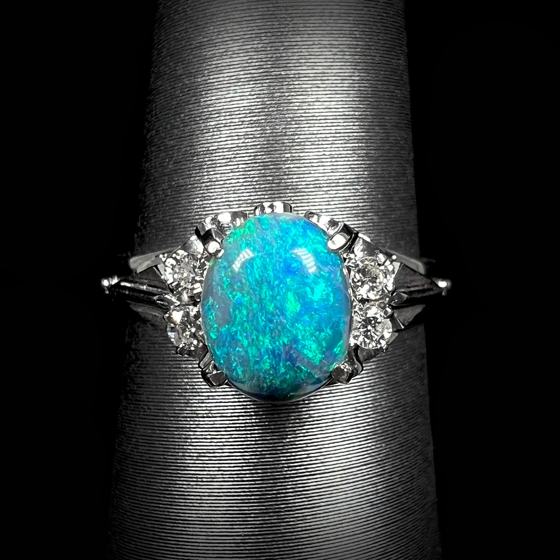 Macro front view of a dainty, 0.89ct black opal engagement ring mounted in platinum with diamond accents.