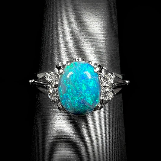 Macro front view of a dainty, 0.89ct black opal engagement ring mounted in platinum with diamond accents.