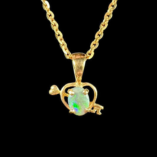 An 18 karat yellow gold heart and key design pendant set with an oval cut Australian black opal.