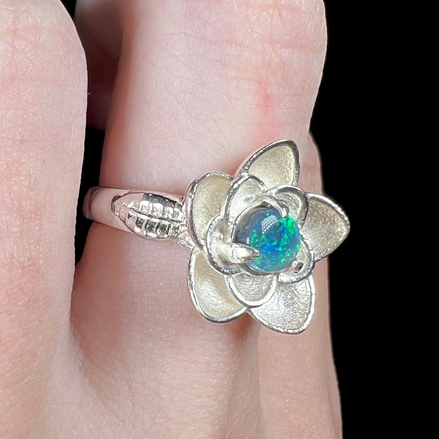 Black opal lotus flower design ring in textured sterling silver shown close-up from angle on finger