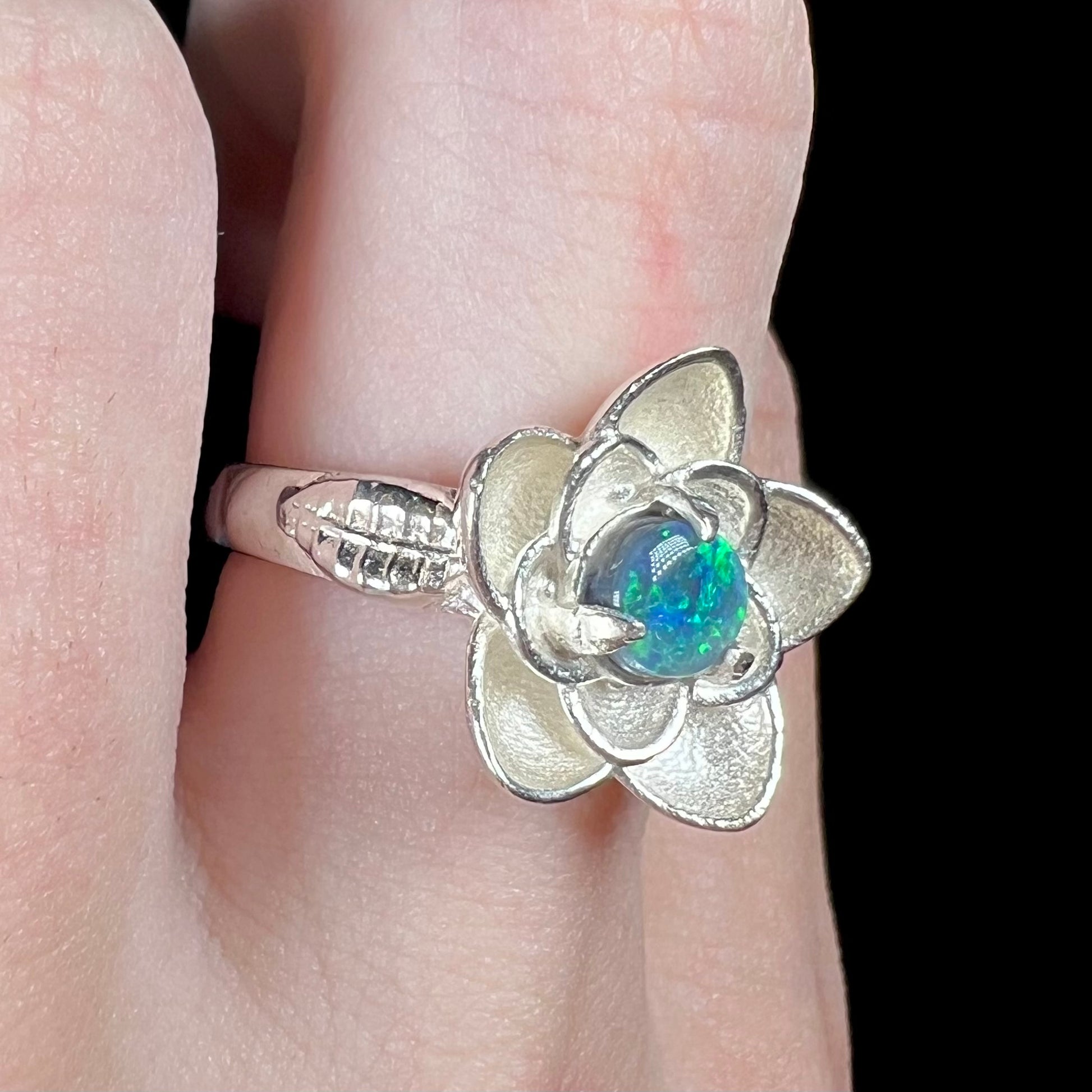 Black opal lotus flower design ring in textured sterling silver shown close-up from angle on finger