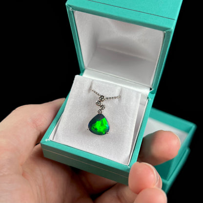 A black opal and diamond necklace held in a blue pendant box at an angle, revealing its bright green flash.