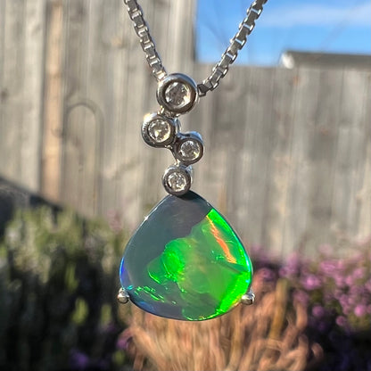 A macro close-up of a black opal and diamond necklace outdoors, showing a moderate green flash with a red stripe.