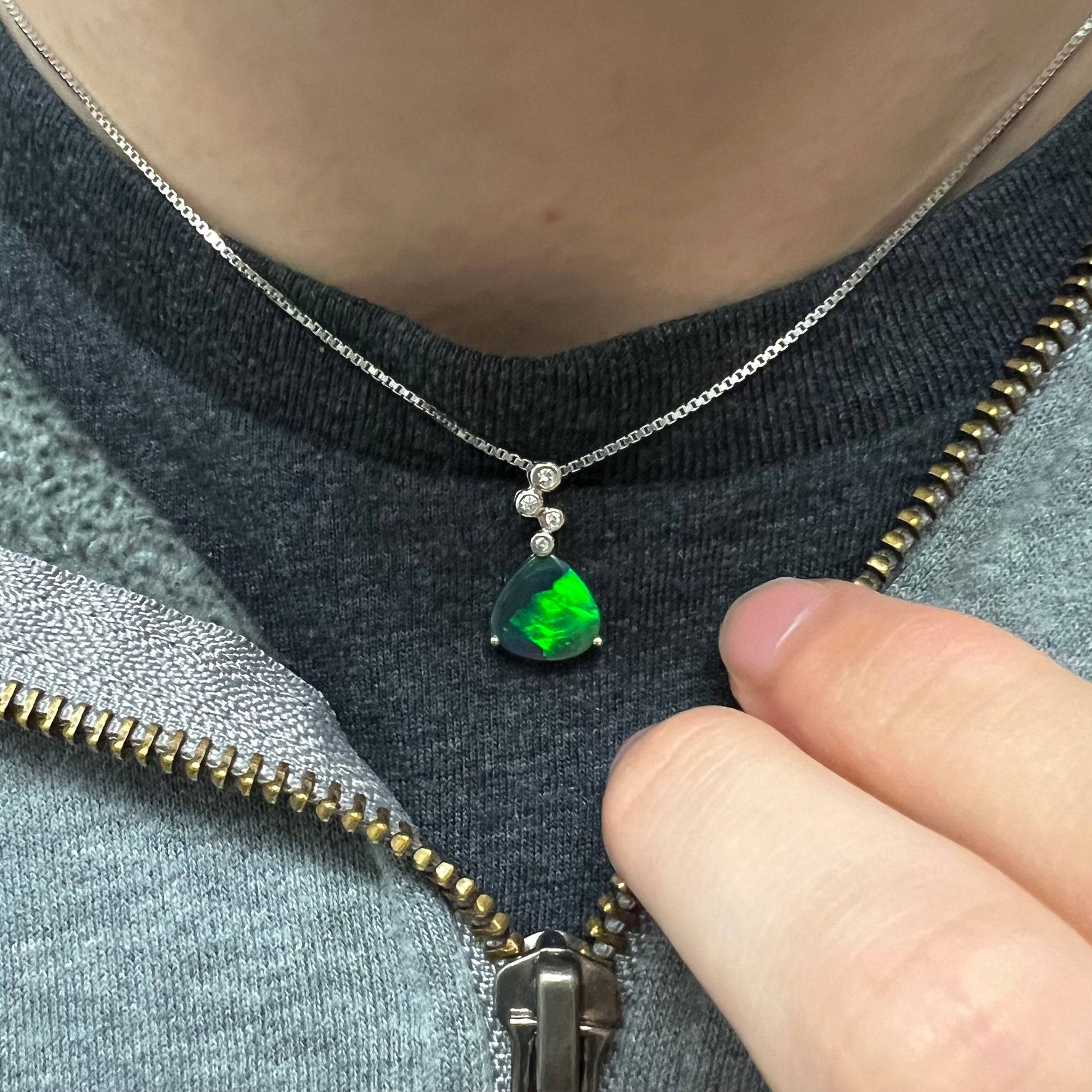 A black opal and diamond necklace worn around the neck on a black T-shirt, showing a bright green flash.