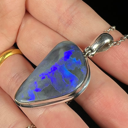 Black opal pendant in sterling silver with bright blue flashes of color regimented in color bars, held flat in hand