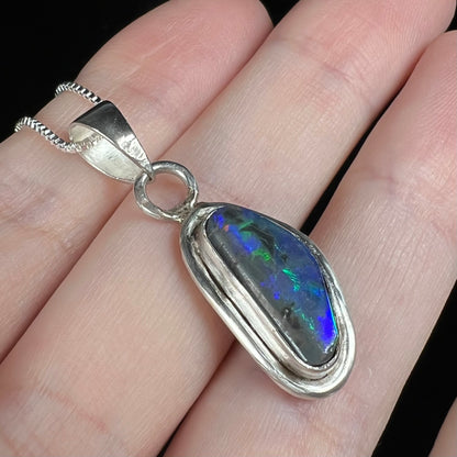 Angled close-up of a handmade sterling silver black opal pendant with blue and green colors in the opal.