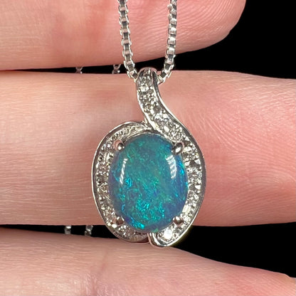 Macro view of a black opal pendant held in a hand, soft blue play-of-color is seen across the opal's surface.