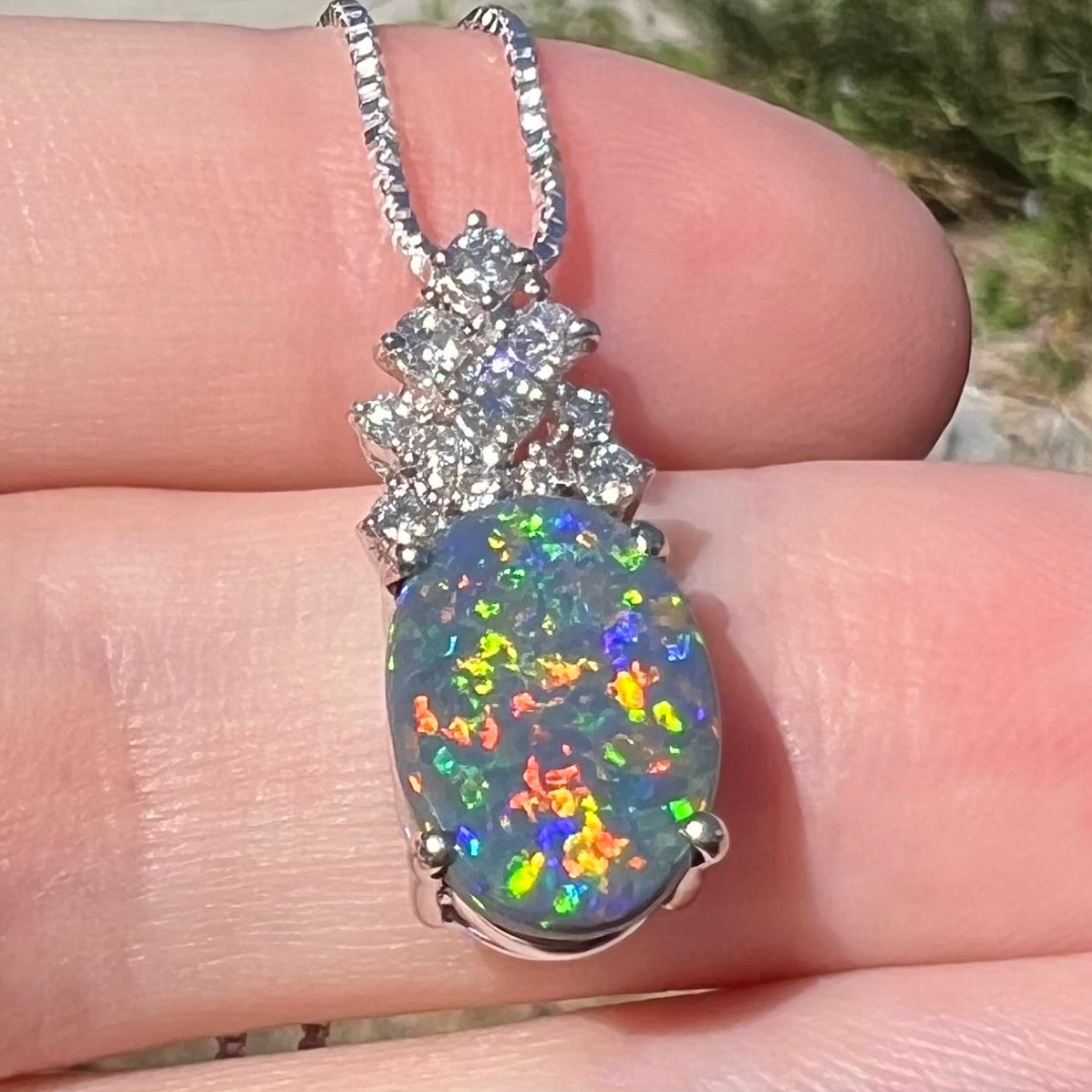 Vibrant multicolor flashes of red, orange, green, and blue play-of-color seen in Australian black opal pendant, viewed in sunlight close-up from bottom angle.