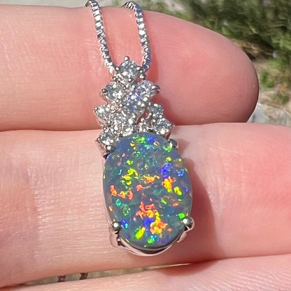 Vibrant multicolor flashes of red, orange, green, and blue play-of-color seen in Australian black opal pendant, viewed in sunlight close-up from bottom angle.