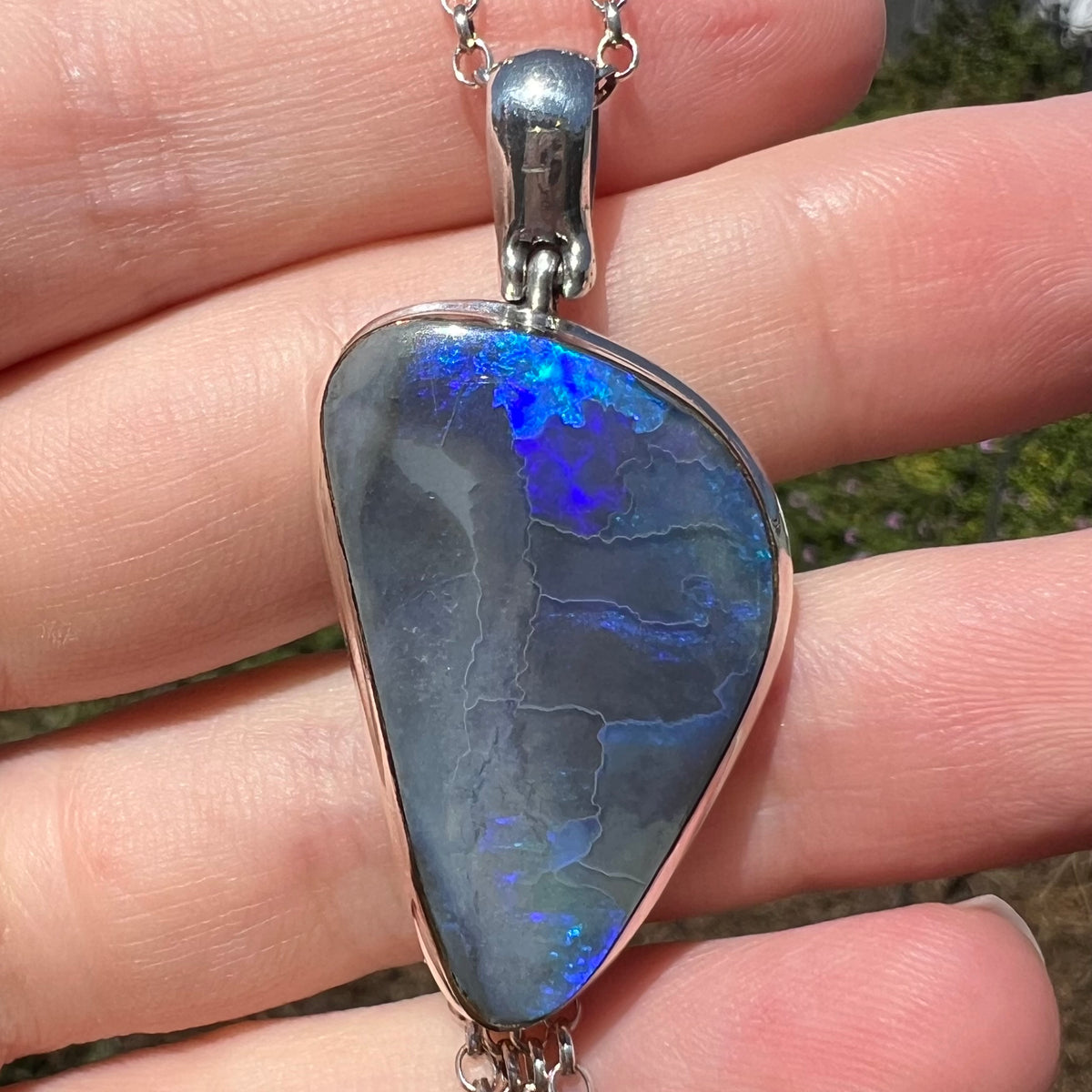 Macro view of silver black opal pendant with blue flashes of color, held in hand under natural sunlight