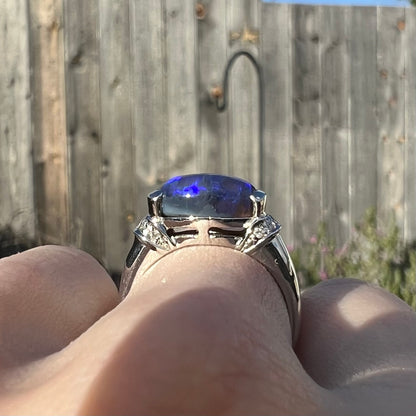 Gallery view of a black opal platinum ring worn on a hand in the sunlight.