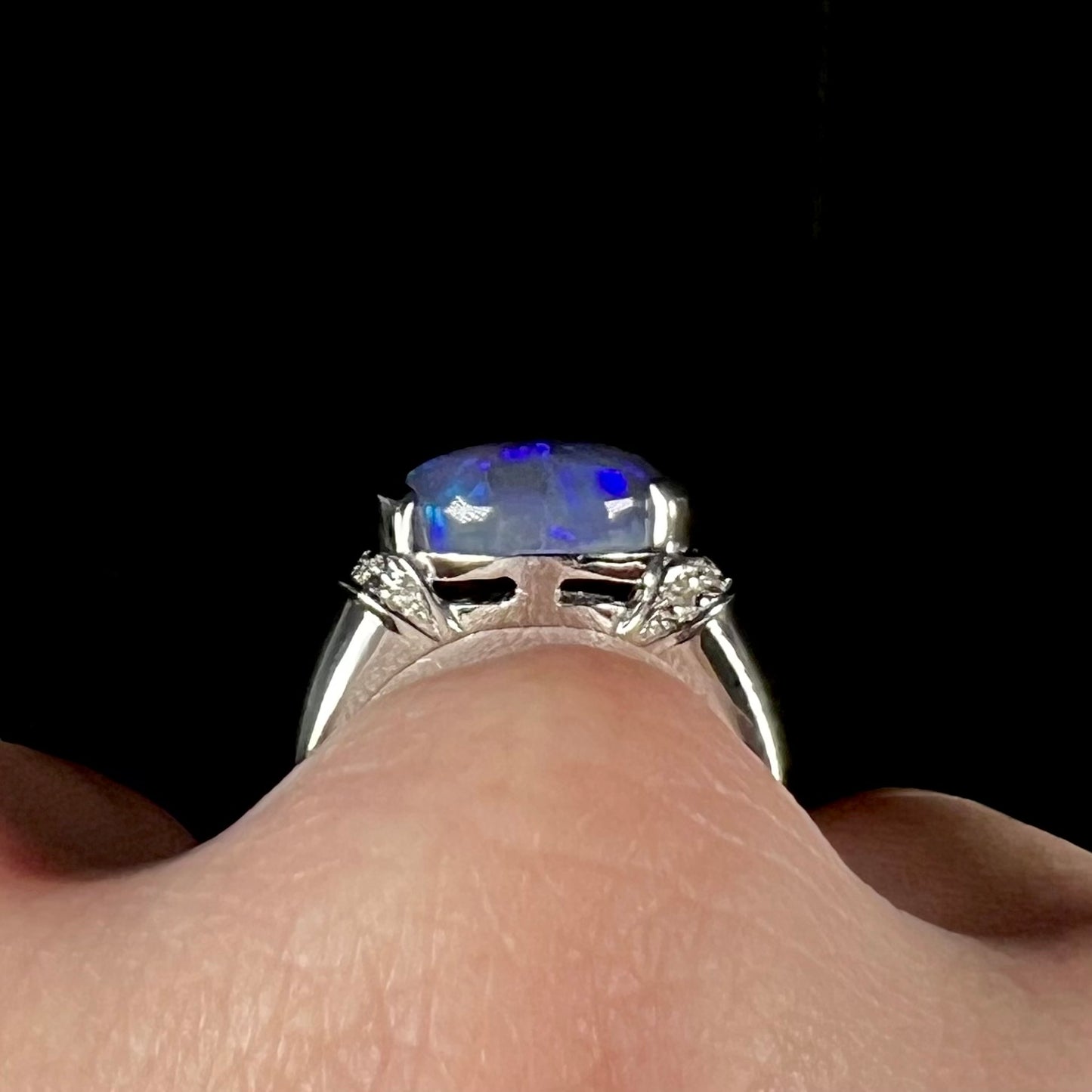 Gallery view of a black opal platinum ring worn on a finger.  The opal's blue edges are exposed.