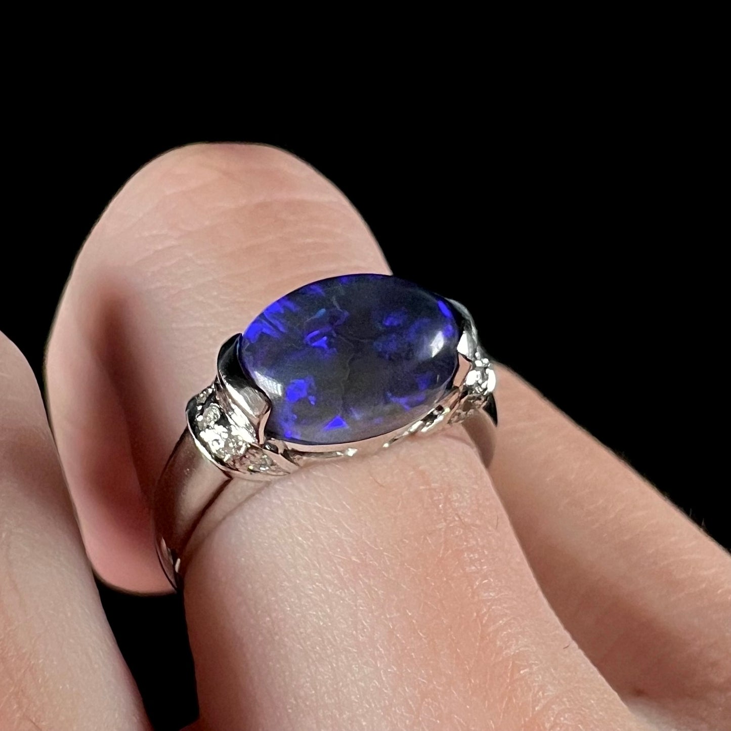 A platinum black opal and diamond ring.  The opal is set East-West in a half bezel.