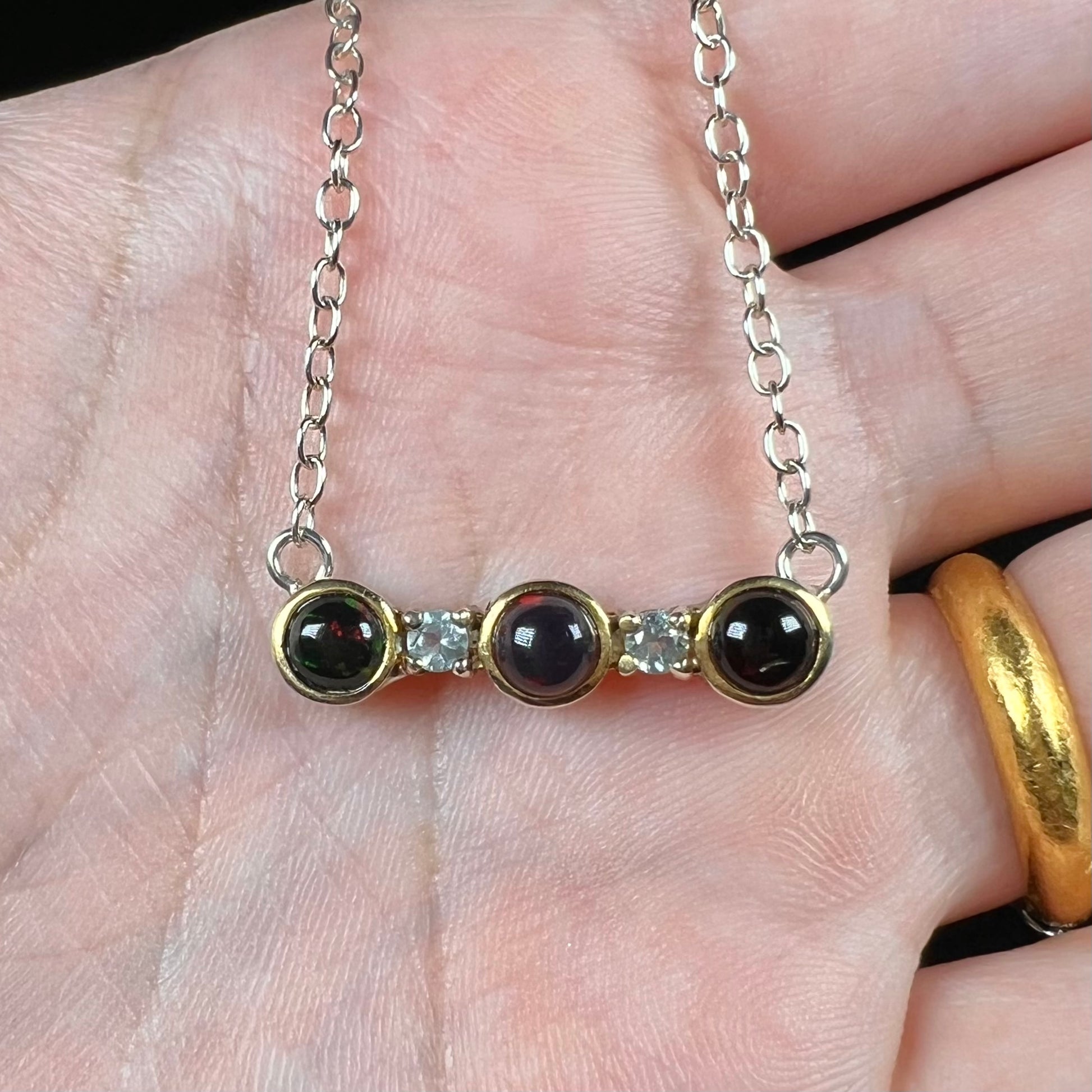 A three-stone black Ethiopian opal and white topaz necklace in two-tone sterling silver.