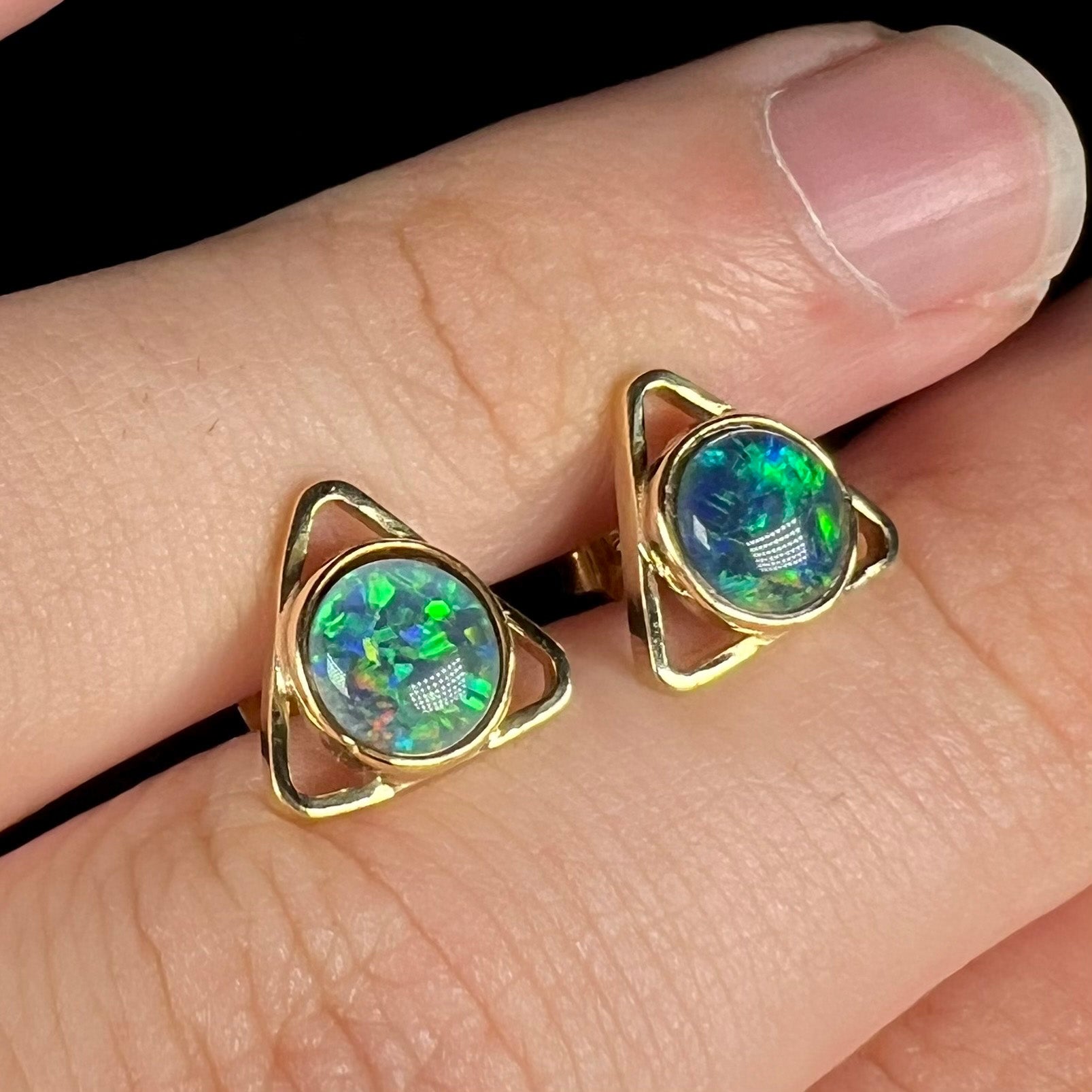 Angled view of two black opal triplet earrings with a triangle shaped design, resting on top of a hand.