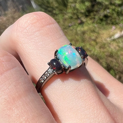 Close-up of black rhodium plated silver ring set with three opals and CZs, worn on finger in sunlight