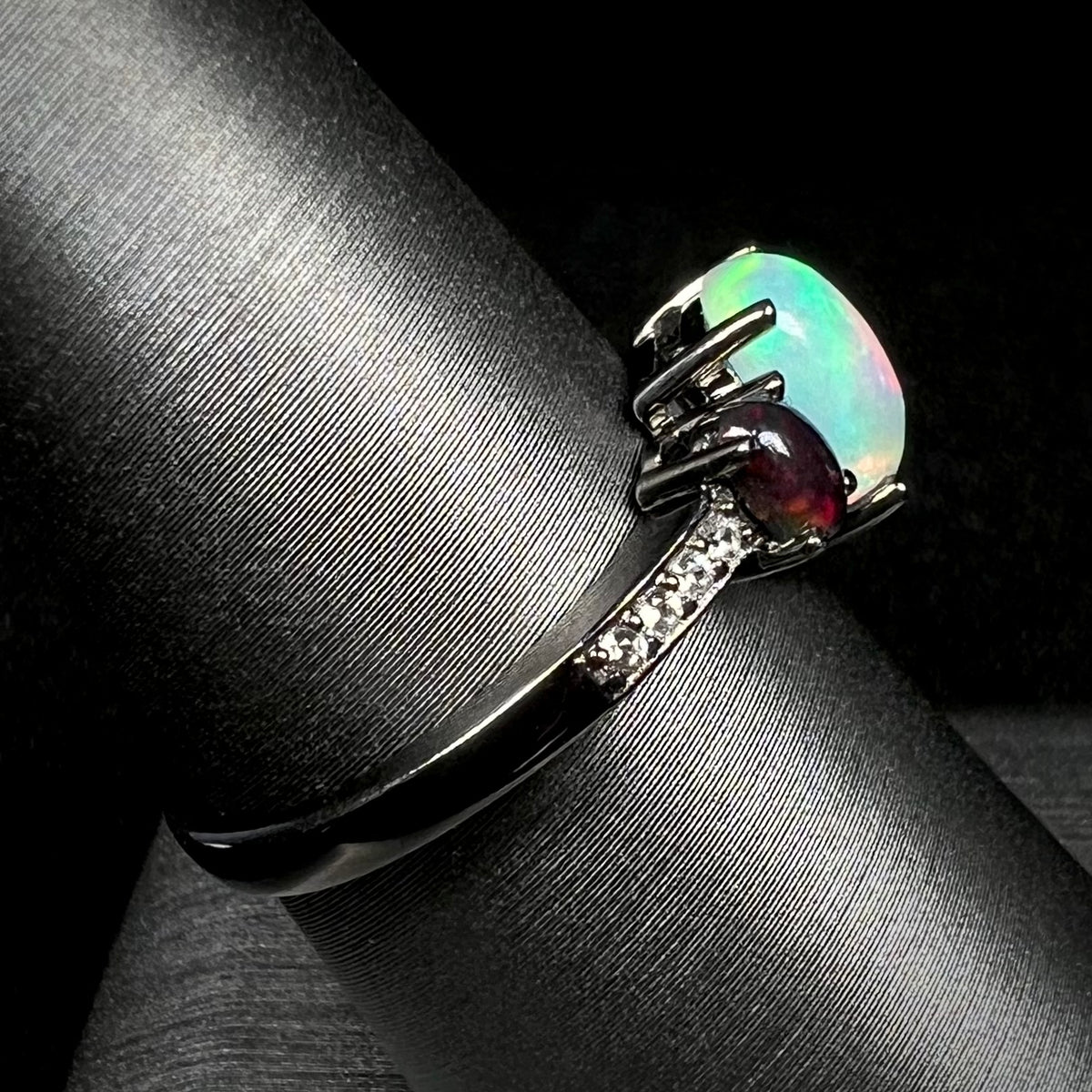 Black rhodium plated sterling silver opal ring with CZ accents on display, shown from side view