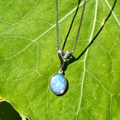 An oval cut black opal doublet necklace set in sterling silver with white zircon accent stones.