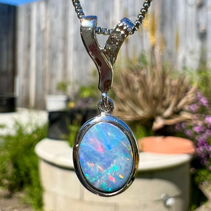 An oval cut black opal doublet necklace set in sterling silver with white zircon accent stones.