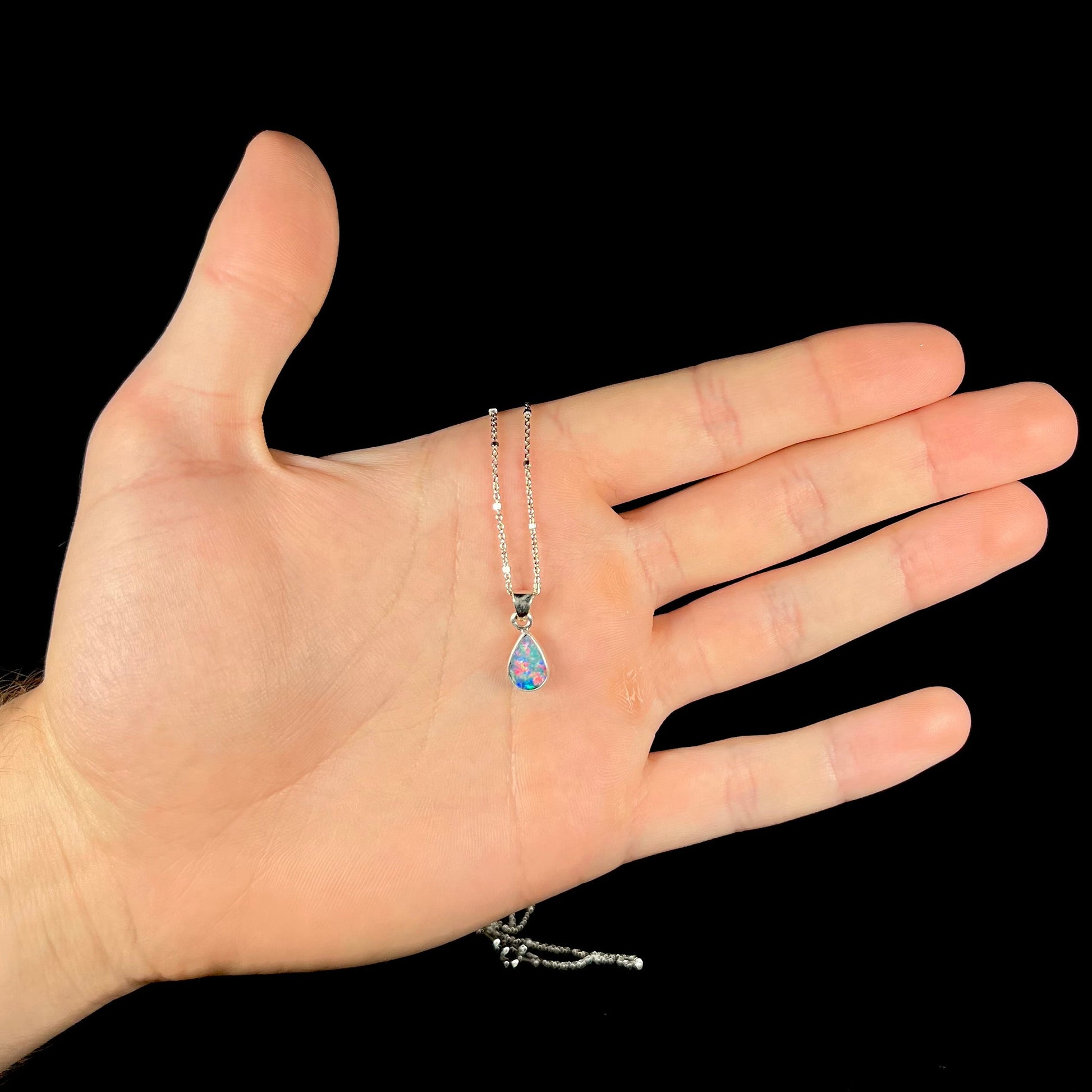 A pear shaped black opal necklace set in sterling silver.  The opal vividly flashes every color of the rainbow.