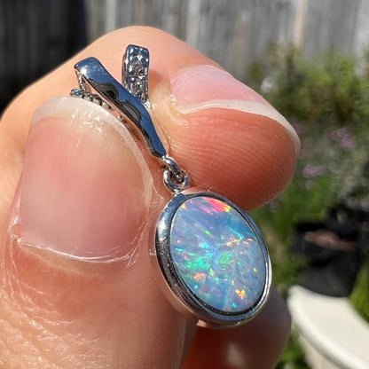 An oval cut black opal doublet necklace set in sterling silver with white zircon accent stones.