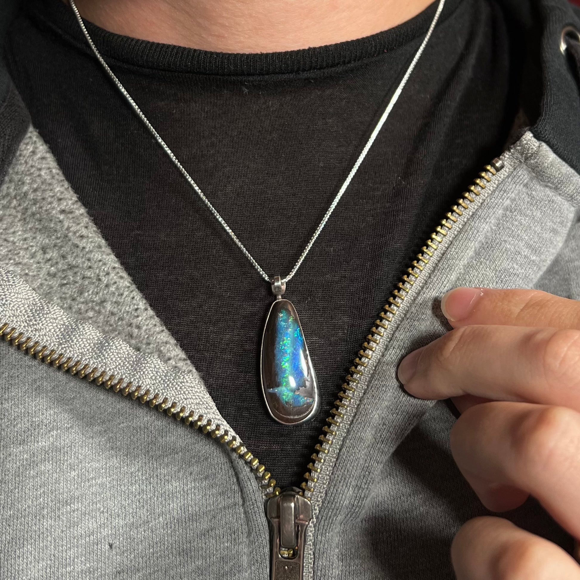 A blue Australian boulder opal necklace in sterling silver, worn around a neck against a dark shirt.