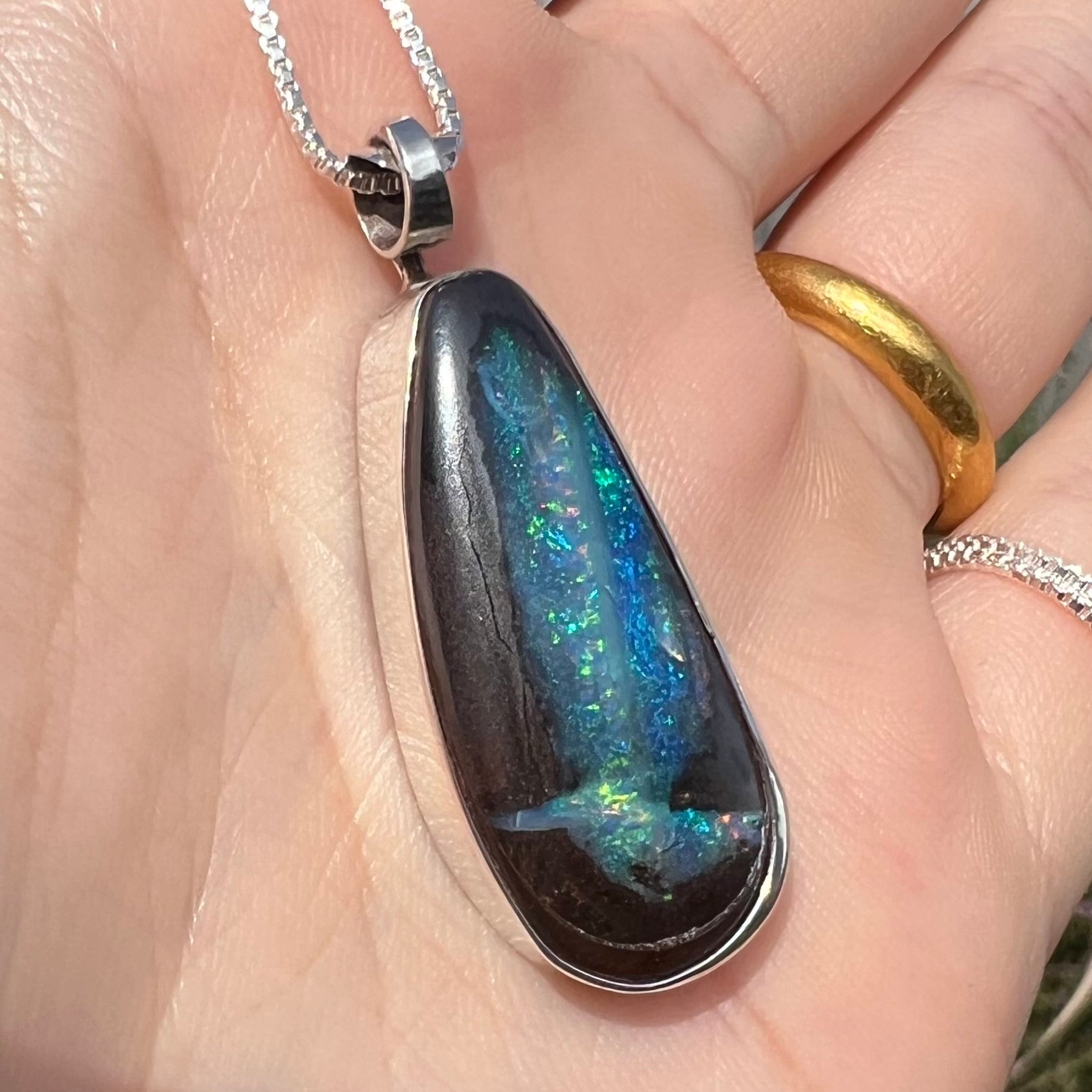 Angled close-up of an Australian boulder opal pendant with glittering blue-green color play in sunlight.