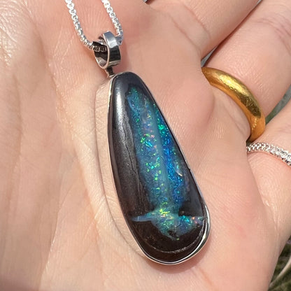 Angled close-up of an Australian boulder opal pendant with glittering blue-green color play in sunlight.
