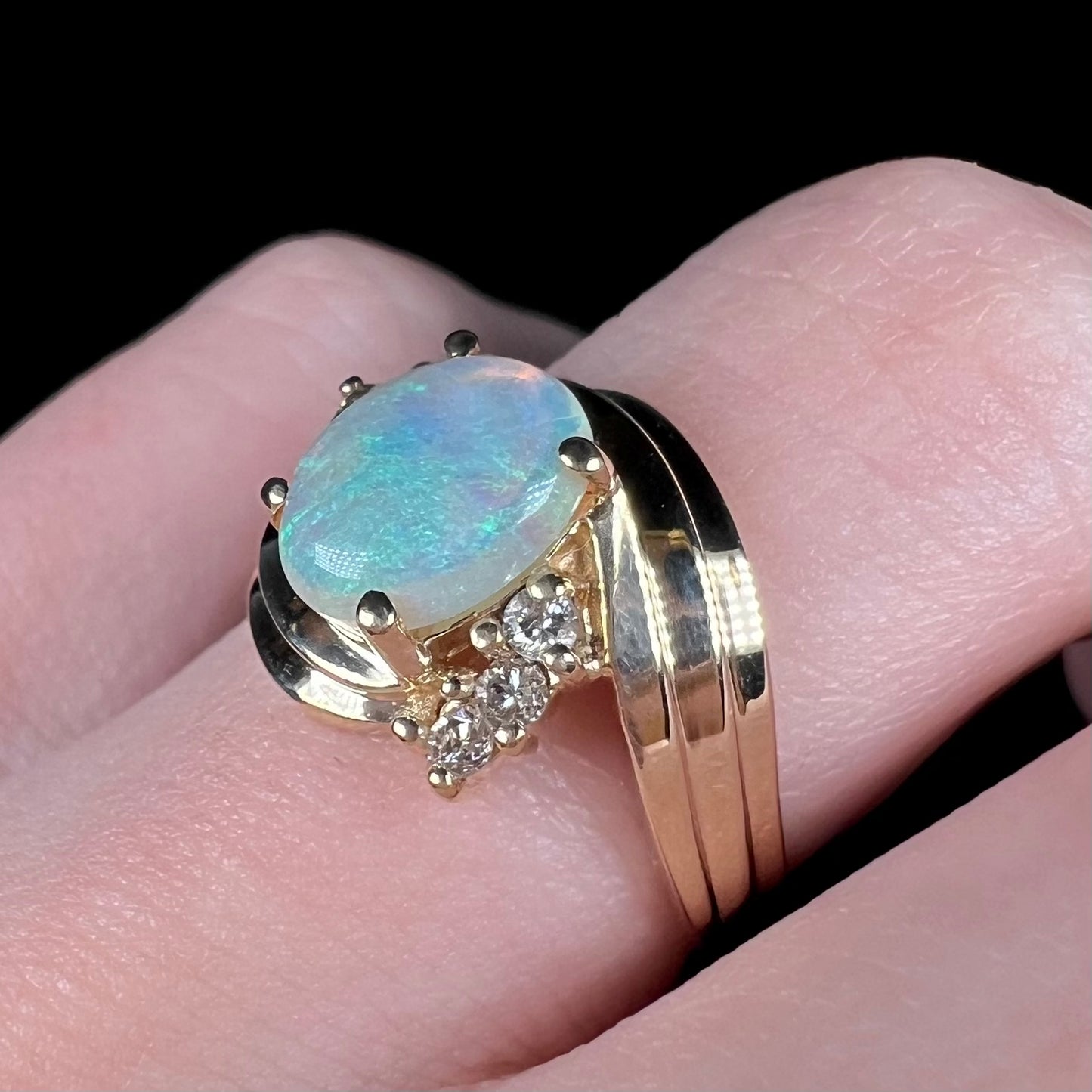 Close-up of subtle blue australian semi-crystal opal and diamond ring in 14k gold, worn on finger