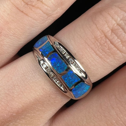 Close-up macro view of blue Australian opal inlay ring with channel-set diamonds in 14k white gold, worn on finger