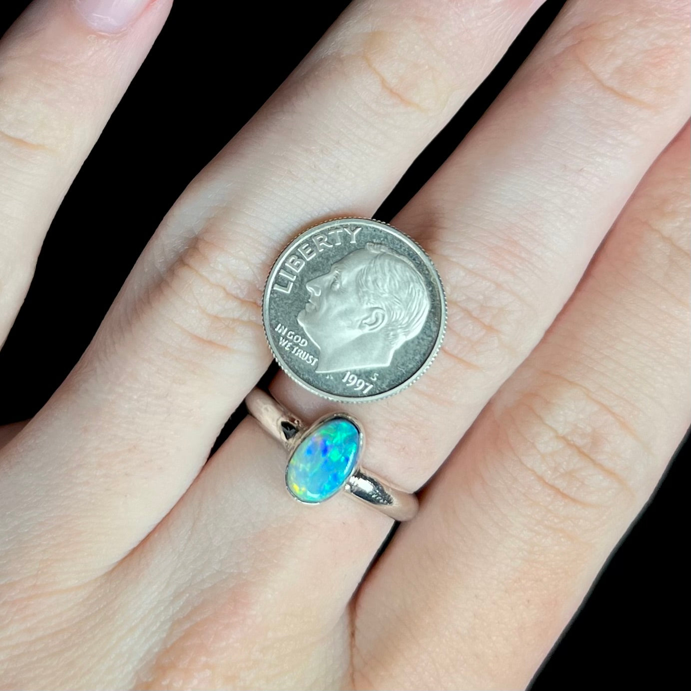 A blue Australian opal solitaire ring made from sterling silver, worn on a hand next to a US dime coin for scale.