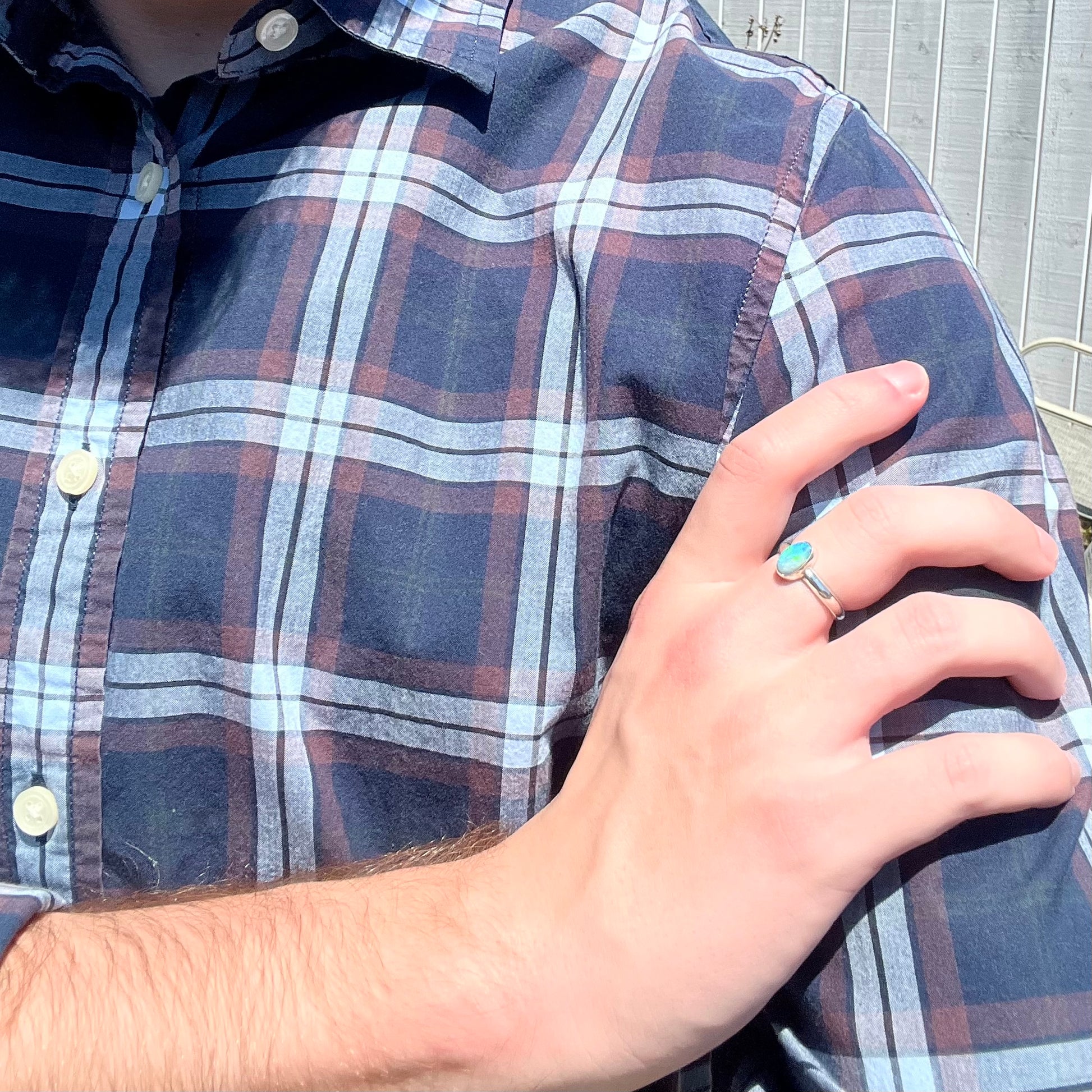 Person resting hand on their opposing shoulder in sunlight while wearing a sterling silver blue Australian opal solitaire ring.