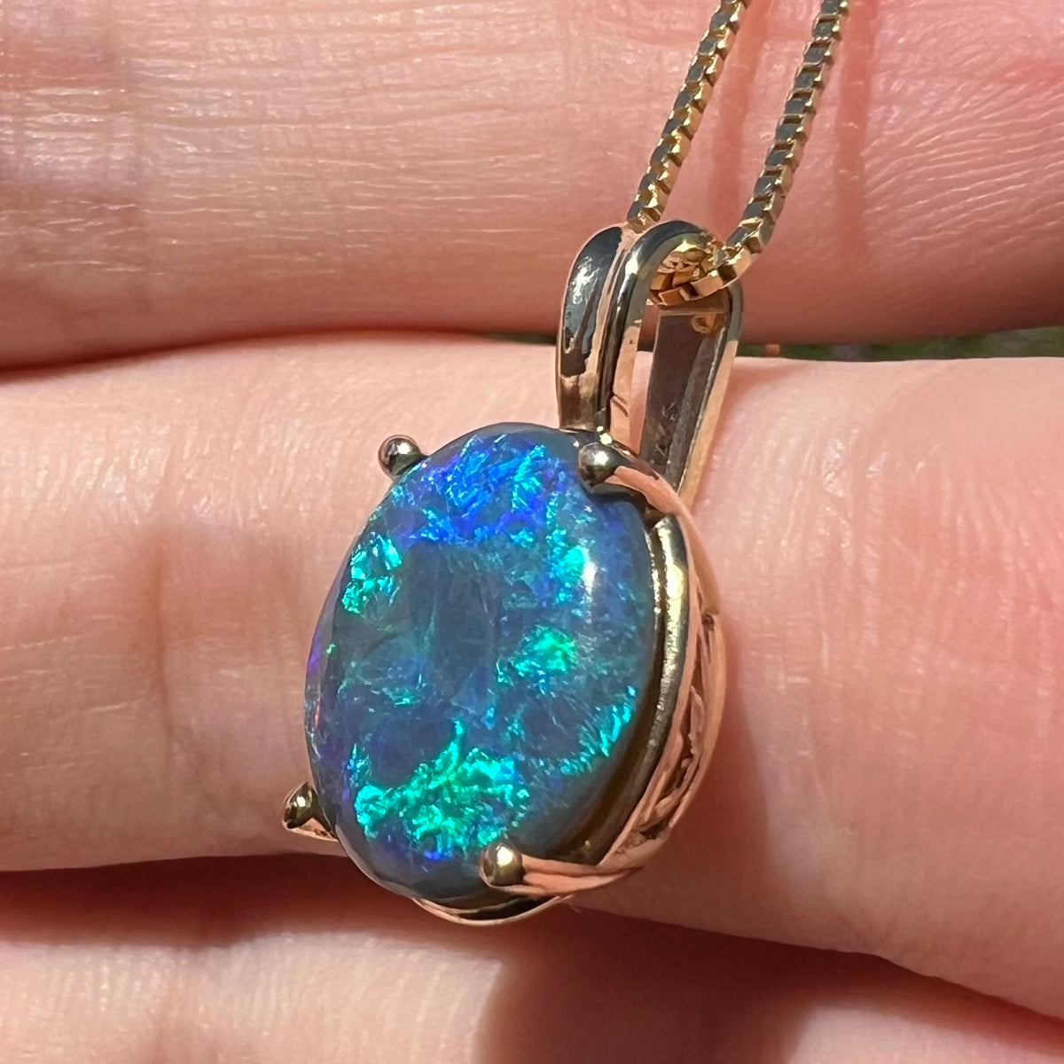 Blue and teal flashes of color seen in Lightning Ridge black opal pendant, shown close-up from angle in natural light
