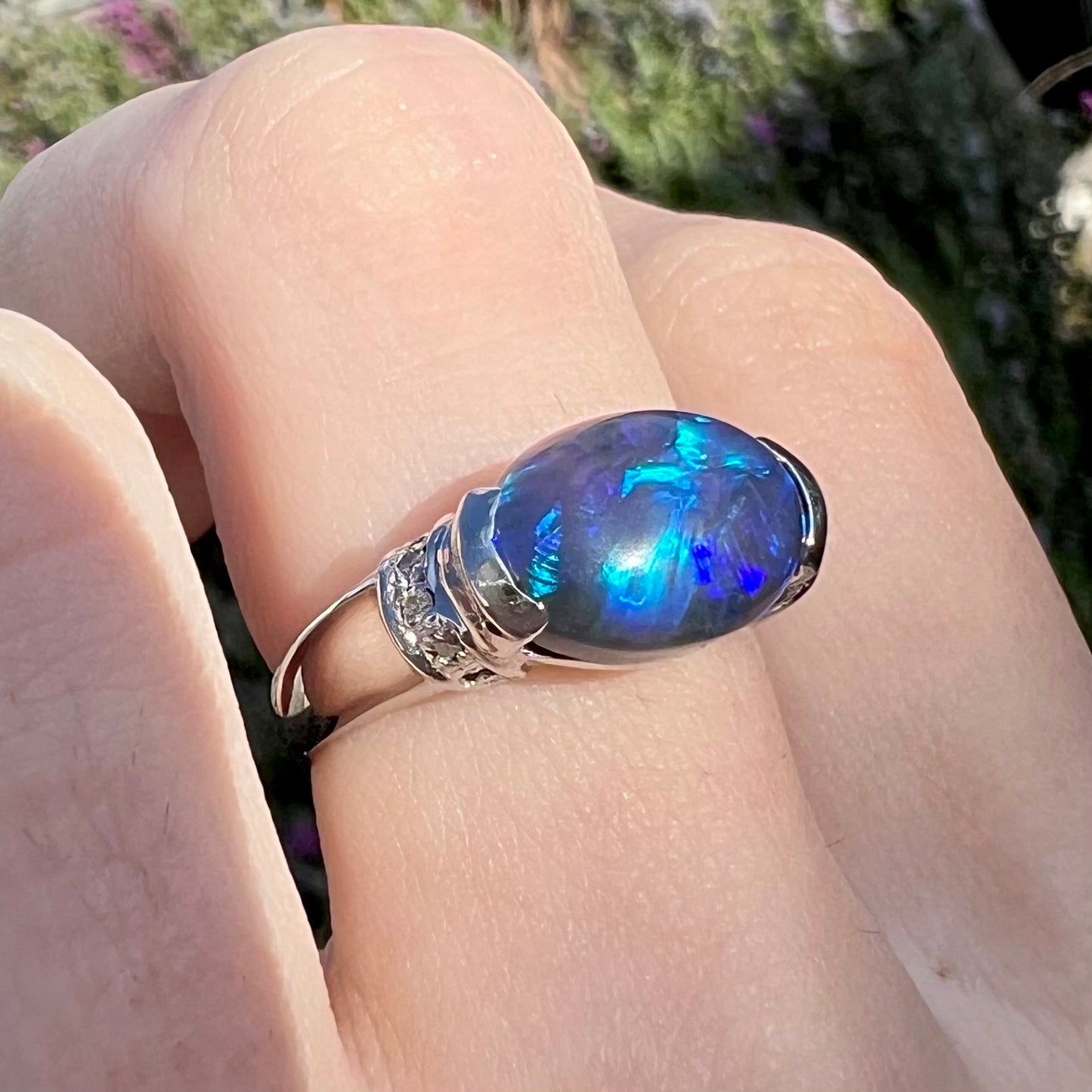 Blue colors are seen in an oval cut black opal ring worn on a finger.