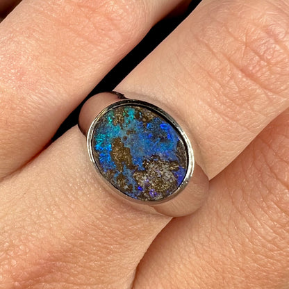 A stainless steel men's Australian boulder opal ring with blue color play, shown close-up on a finger.