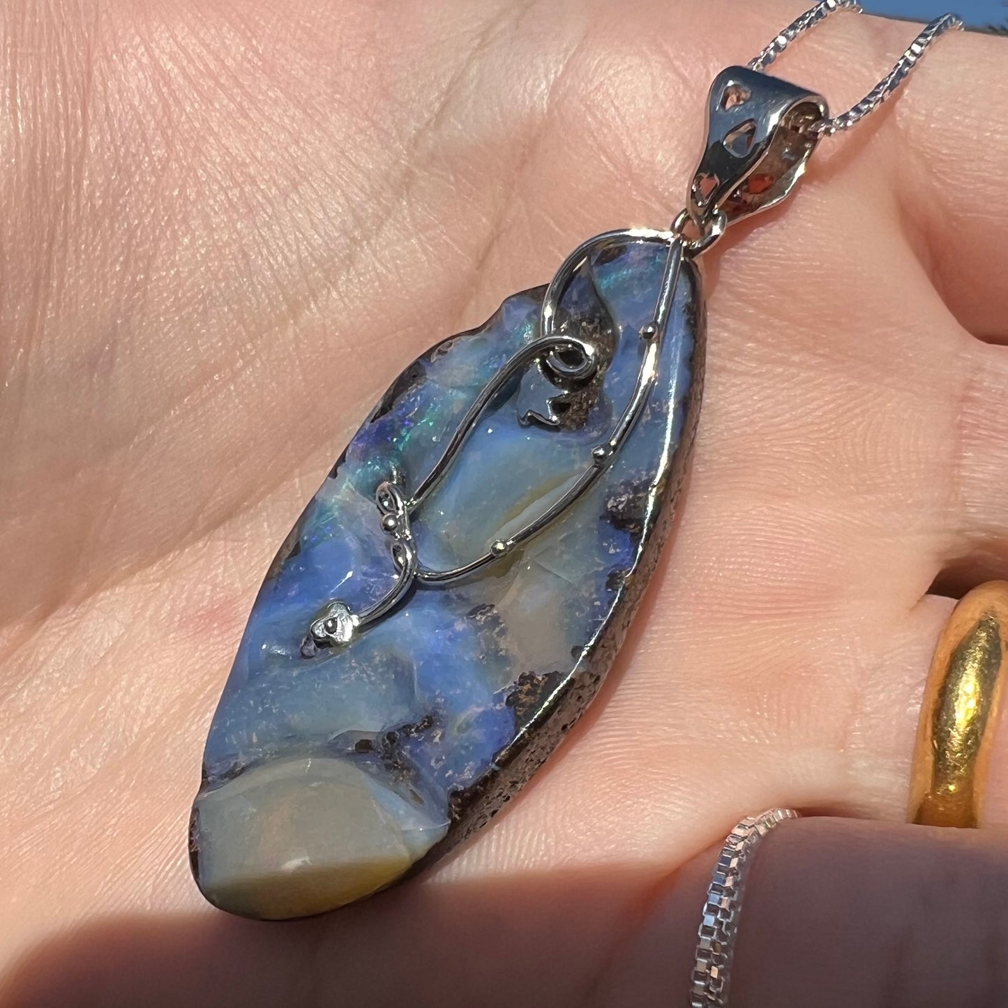 A large, blue Australian boulder opal necklace in sterling silver, shown close-up at an angle in sunlight.