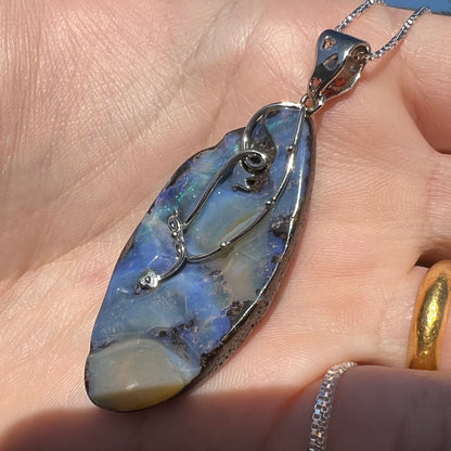 A large, blue Australian boulder opal necklace in sterling silver, shown close-up at an angle in sunlight.