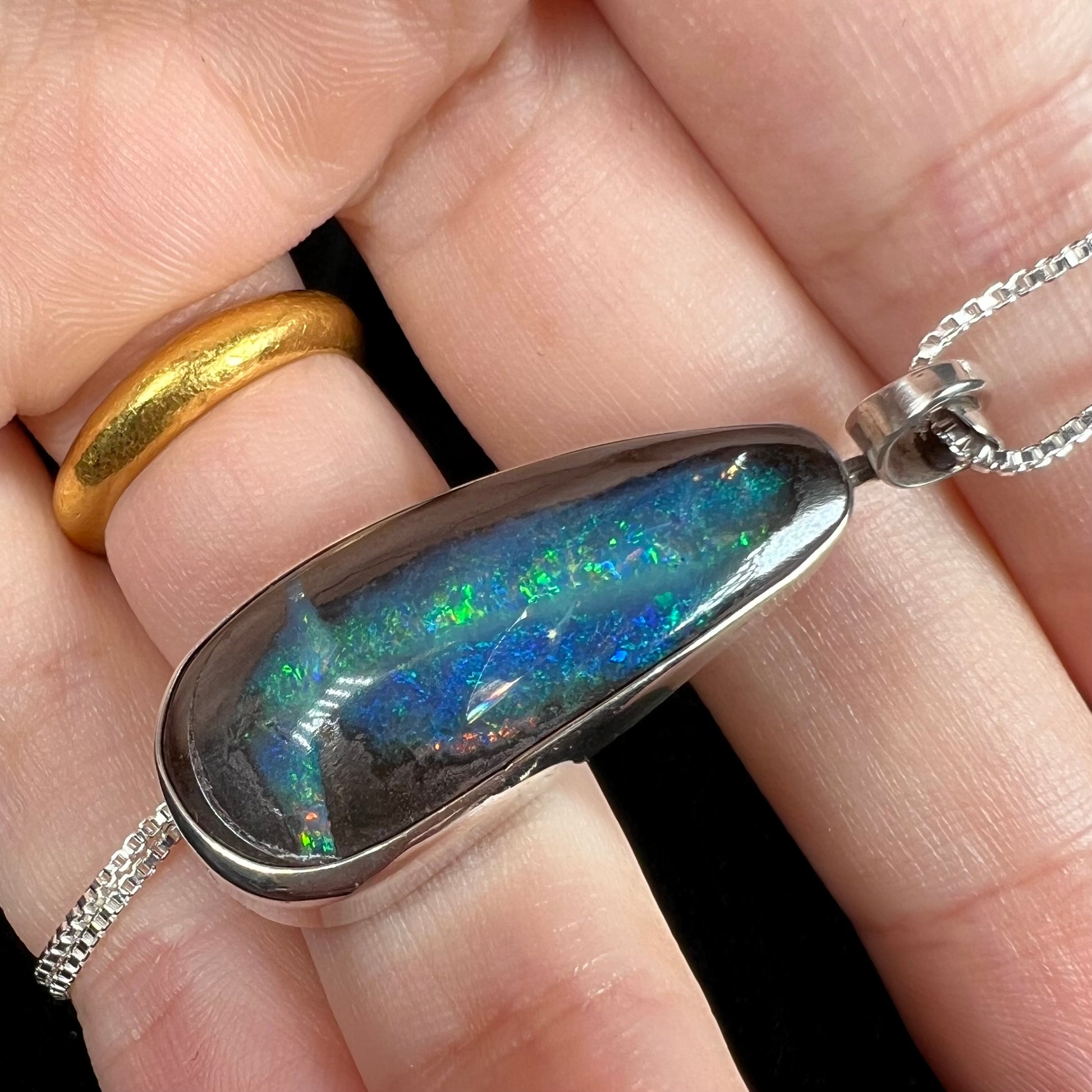 Angled close-up of an Australian boulder opal pendant with blue and green color play, shown in a hand.
