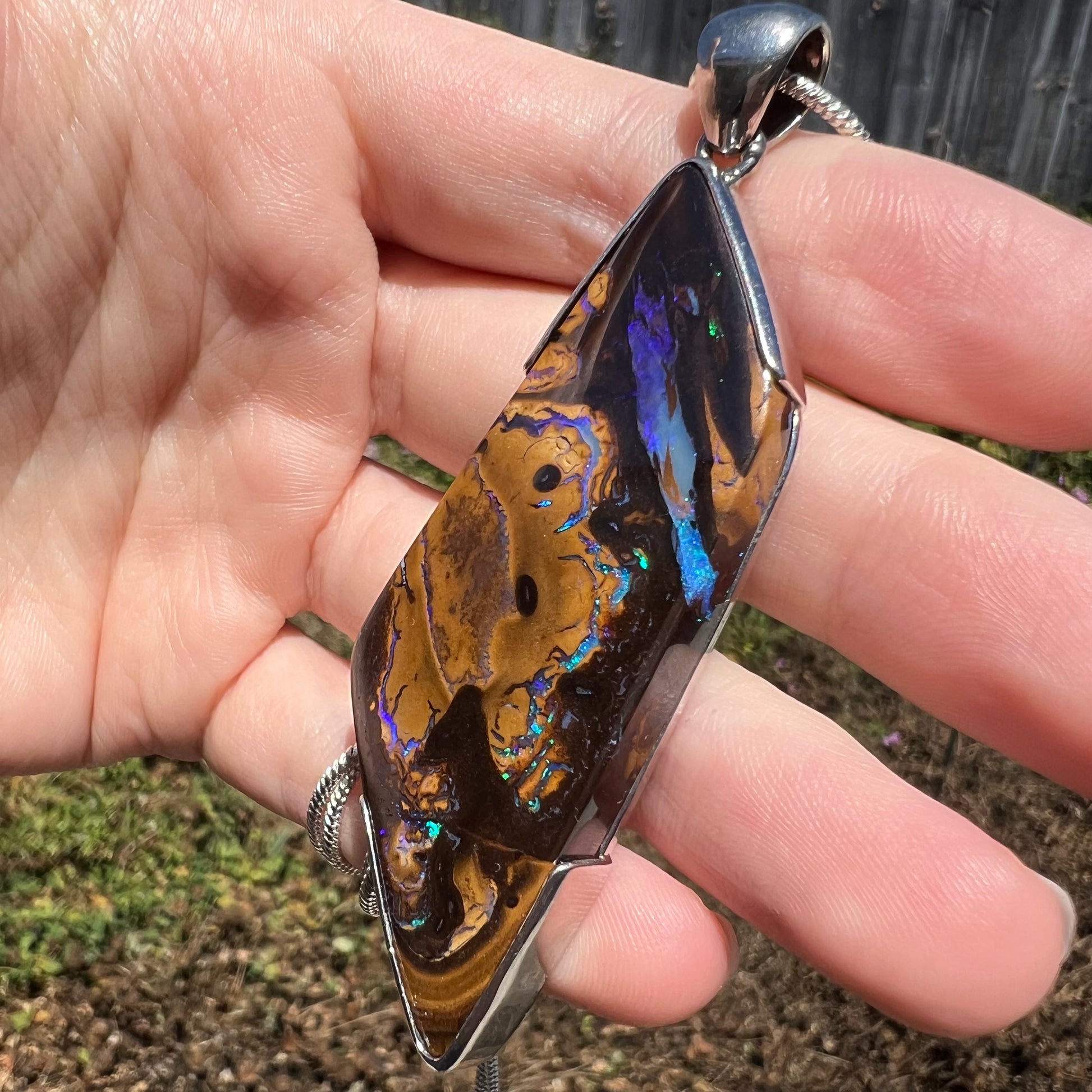 Blue veins seen in boulder opal men's pendant, held in hand under natural sunlight