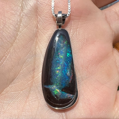Close-up of an Australian boulder opal pendant with glittering blue and green color play, shown in a hand in sunlight.