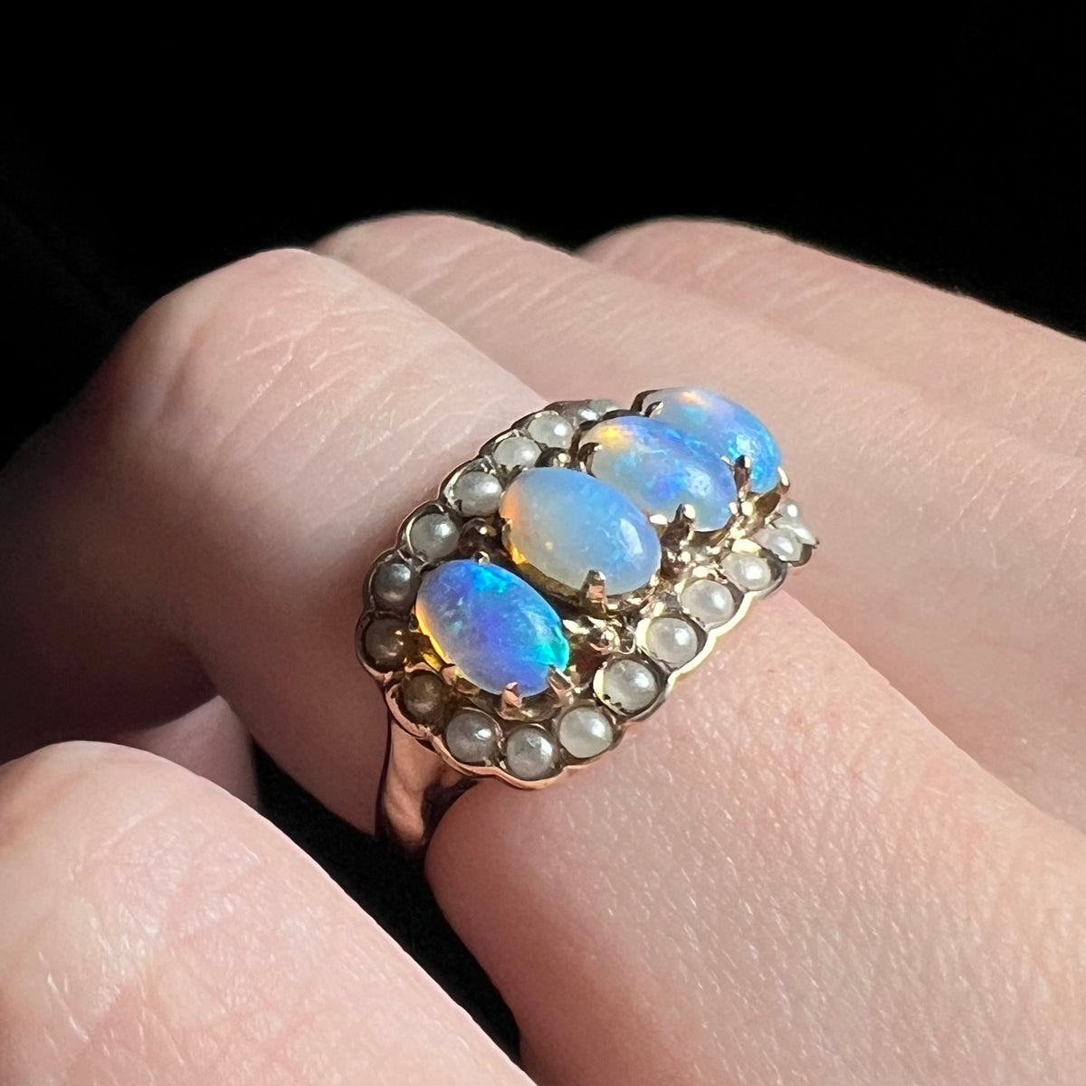 Angled close-up of Victorian ring set with four blue Hungarian crystal opals and seed pearls, worn on finger