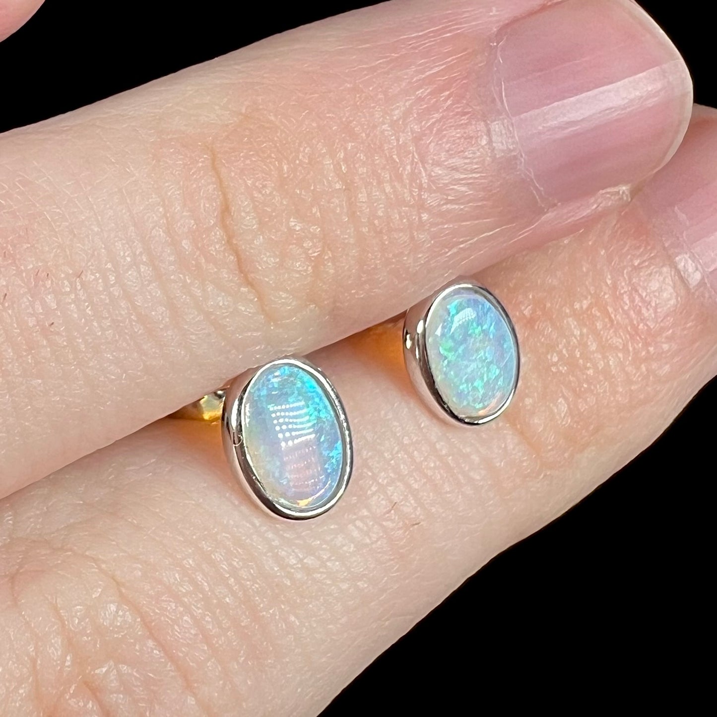 Angled view of blue crystal opal stud earrings in white gold, shown close-up held between two fingers.